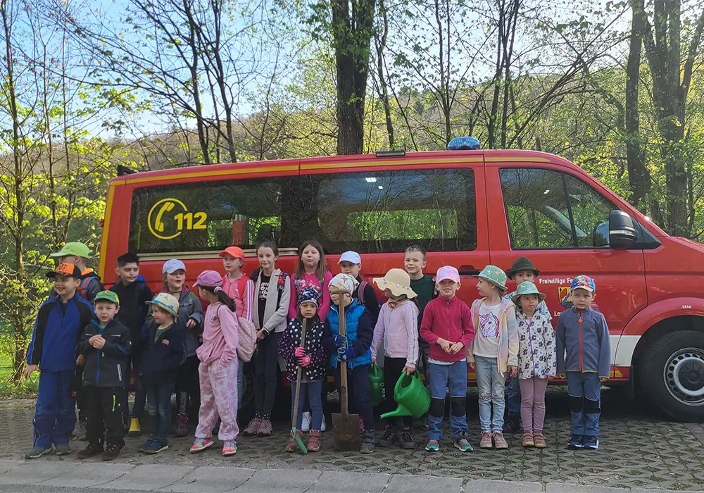 Eine Gruppe von Kindern steht vor einem roten Feuerwehrauto im Freien, einige tragen Hüte und Jacken.