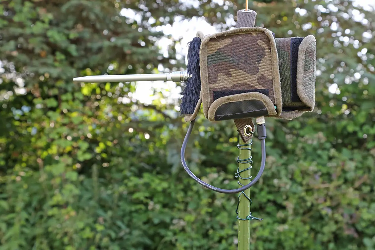 Kleine, tarnfarbene Tasche mit Gummiband an einem Stock befestigt, im Freien mit grünem, verschwommenem Hintergrund.