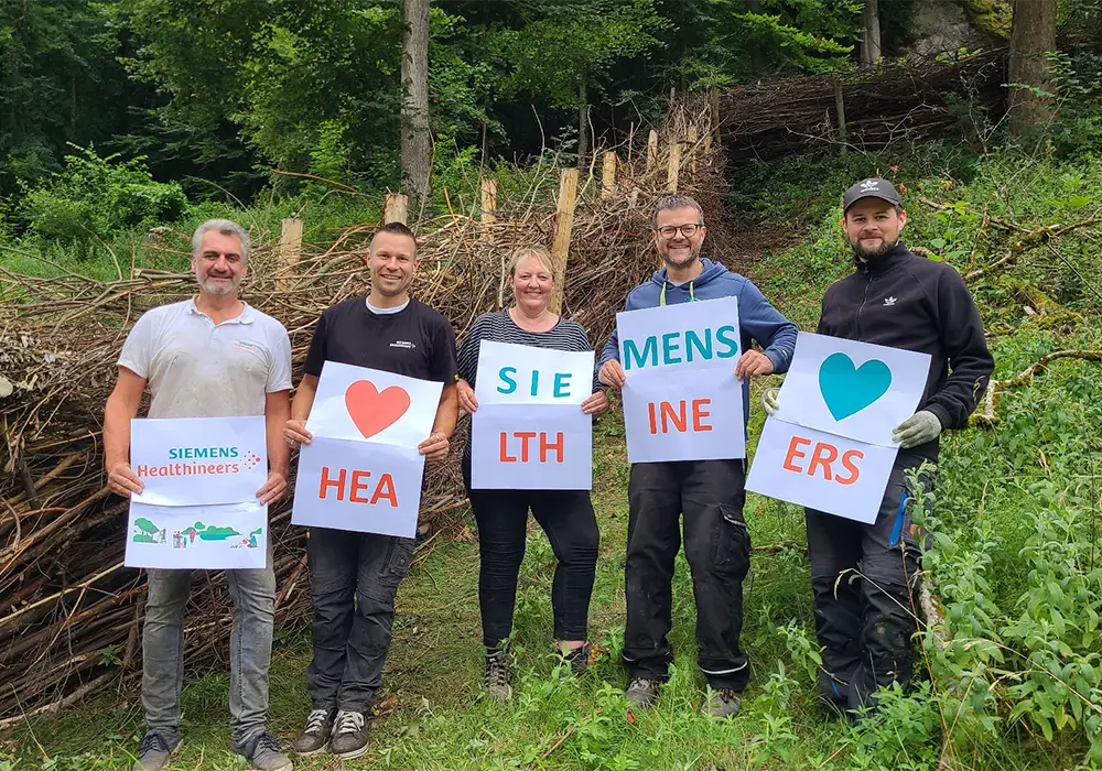 Fünf Menschen stehen im Freien und halten Schilder mit der Botschaft „We love health care workers“ auf Englisch und Deutsch.